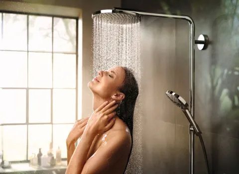Eine Frau genießt eine Dusche unter einer Hansgrohe-Duschbrause, das natürliche Licht durch das Fenster schafft eine beruhigende Atmosphäre.