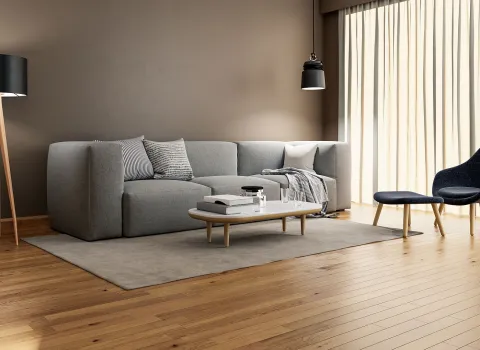 Helles Wohnzimmer mit Holzfußboden, grauem Ecksofa und Designer-Sessel. Der glatte, neutrale Innenputz hebt die elegante Einrichtung hervor.