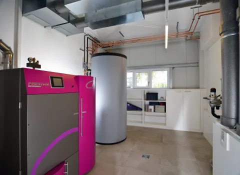 Ein moderner Heizungsraum mit einem auffälligen, pinkfarbenen Heizkessel und einem großen zylindrischen Warmwasserspeicher.
